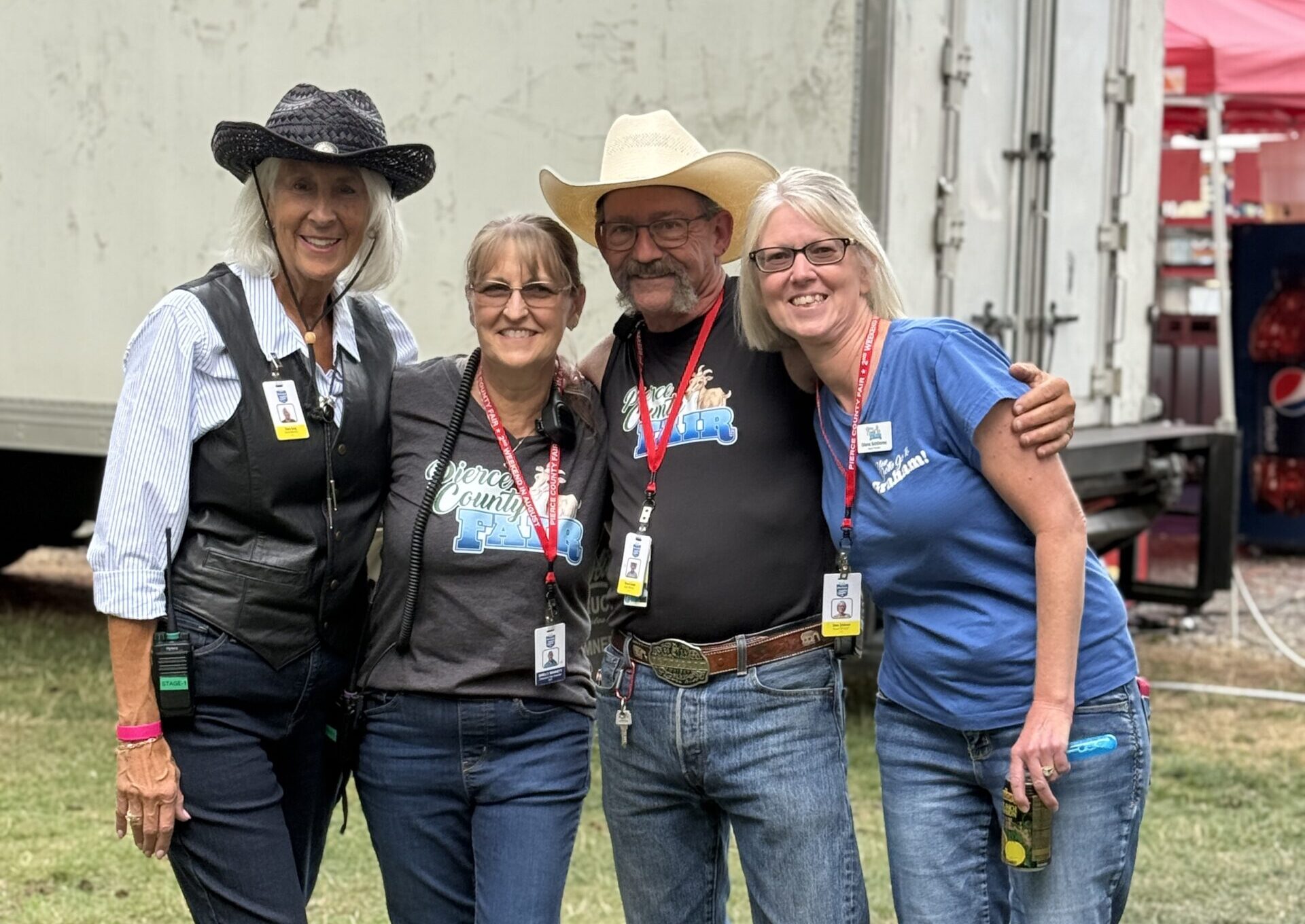 Four Fair staff members wearing event badges pose together outdoors.