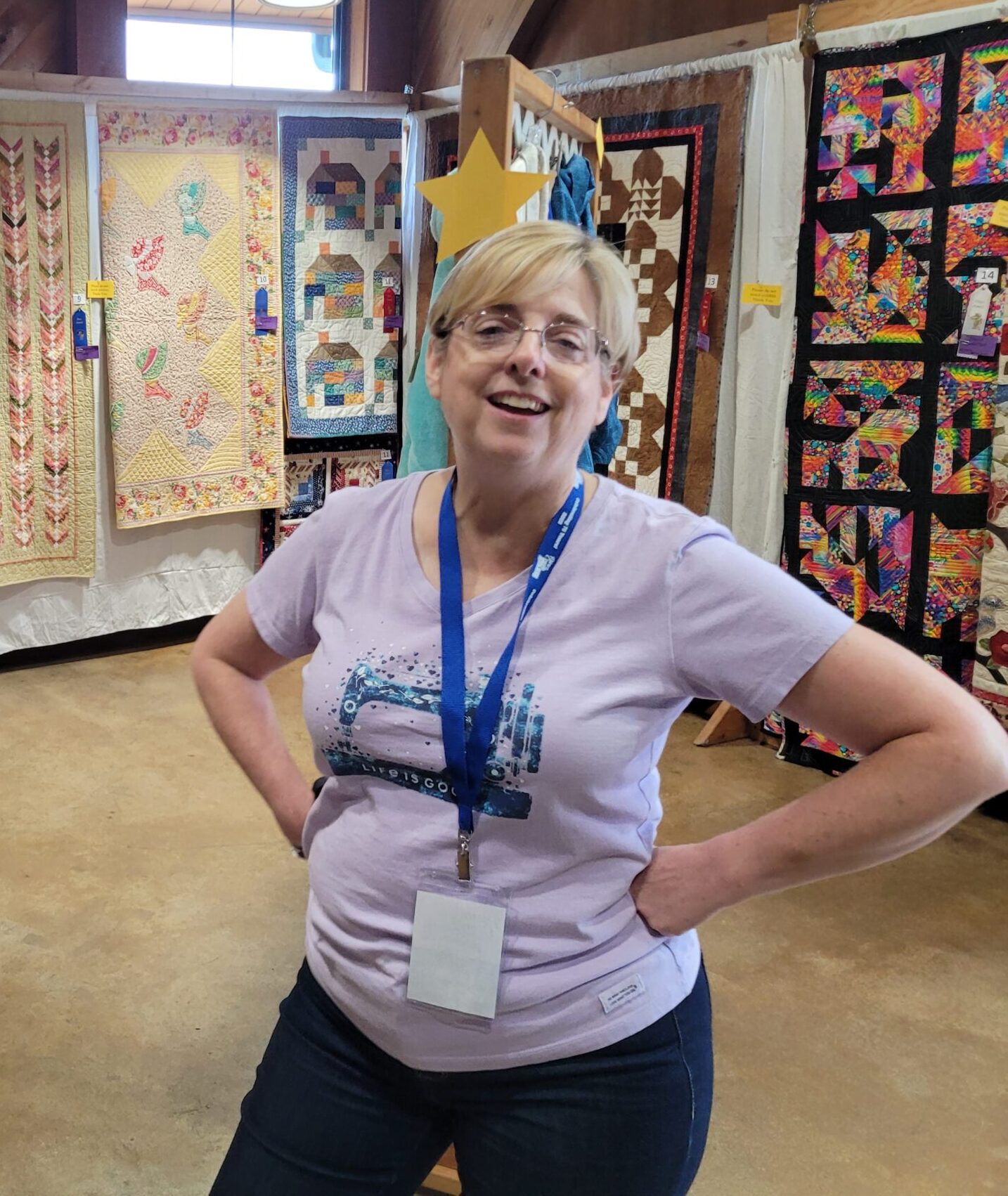 A woman wearing an event badge stands in front of colorful quilt displays.