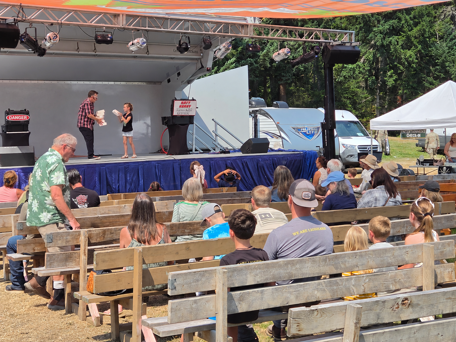 Families watch an outdoor stage performance from rows of benches at the Fair.