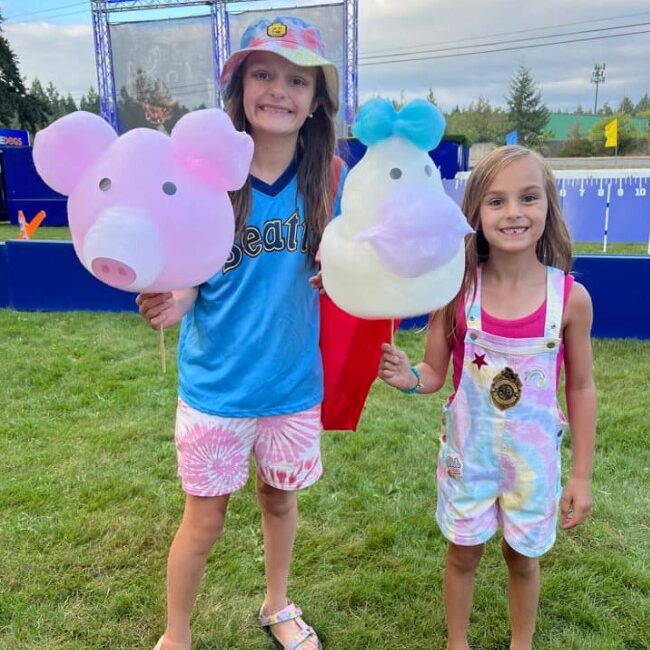Two children smile while holding large animal-shaped cotton candy at the Fair.