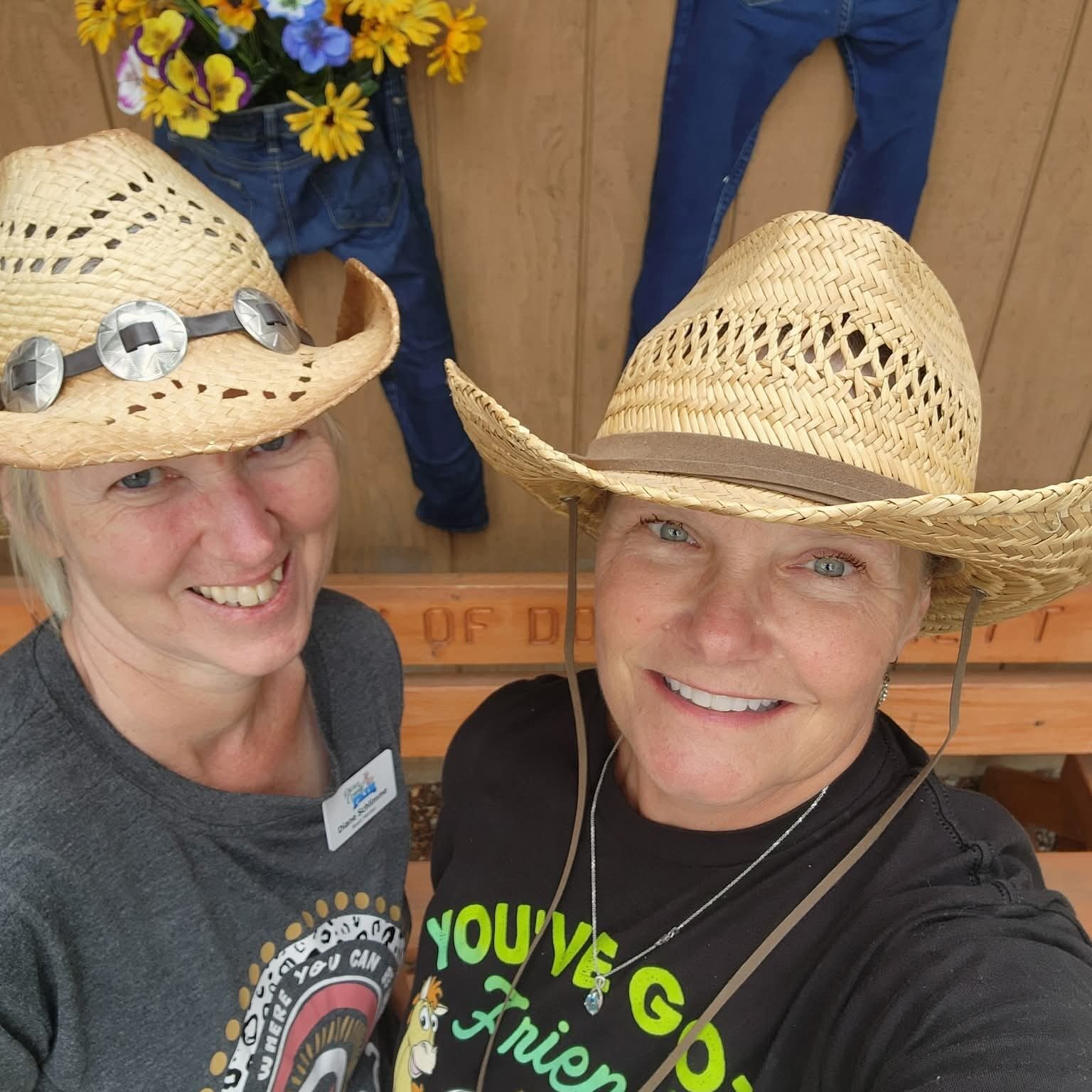 Two women wearing straw hats smile in front of a flower display at the Fair.